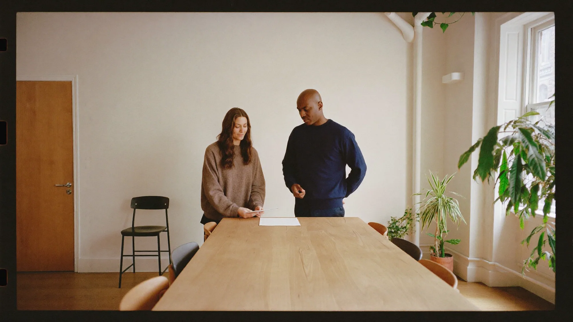A specialist and a client standing over one page at the end of a long table in a bright office